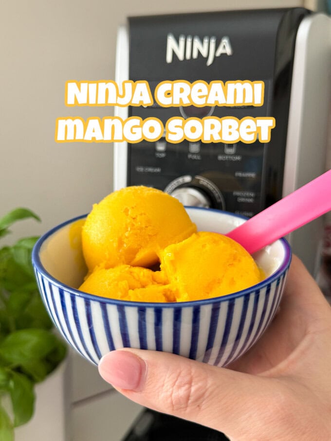3 scoops of mango sorbet in a blue and white striped bowl with a pink spoon in it.