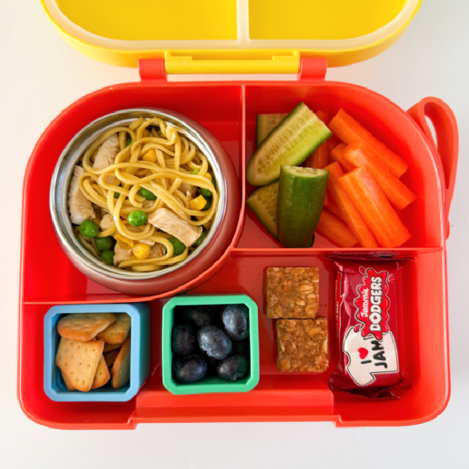 Chicken noodles served in a hot & cold lunch box with sliced carrots and cucumber.