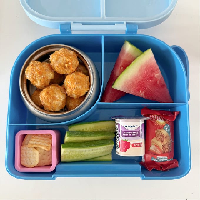 Chicken Sausage bites in a bright blue hot & cold lunch box, served with chunks of watermelon, and other treats.