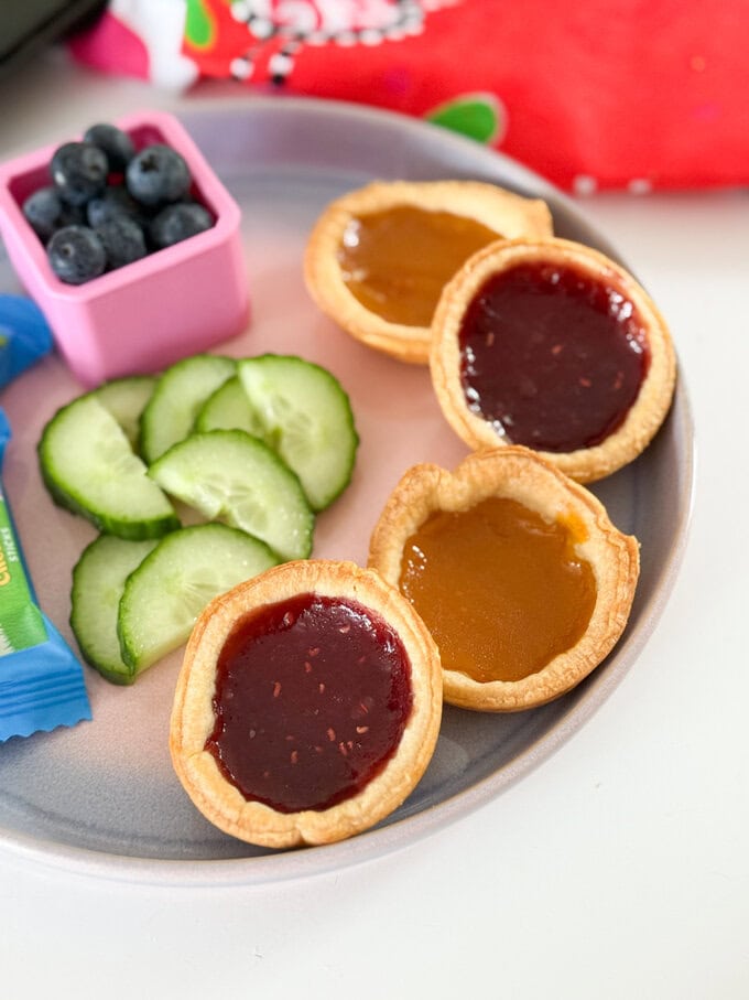 Four Jam Tarts arranged on a plate and served with fresh berries and cucumber slices and cheese chunks.