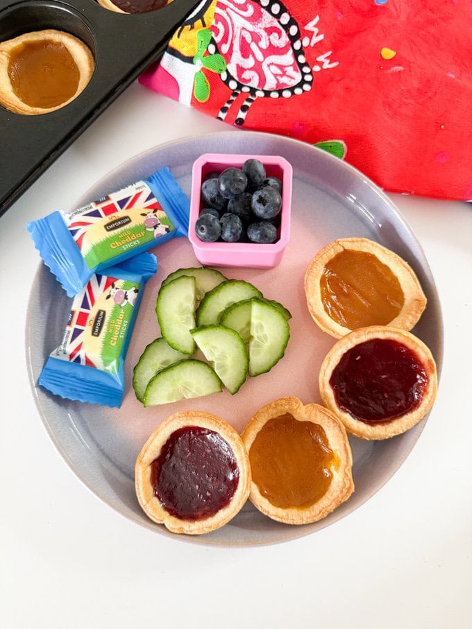 Four Jam Tarts arranged on a plate and served with fresh berries and cucumber slices and cheese chunks.